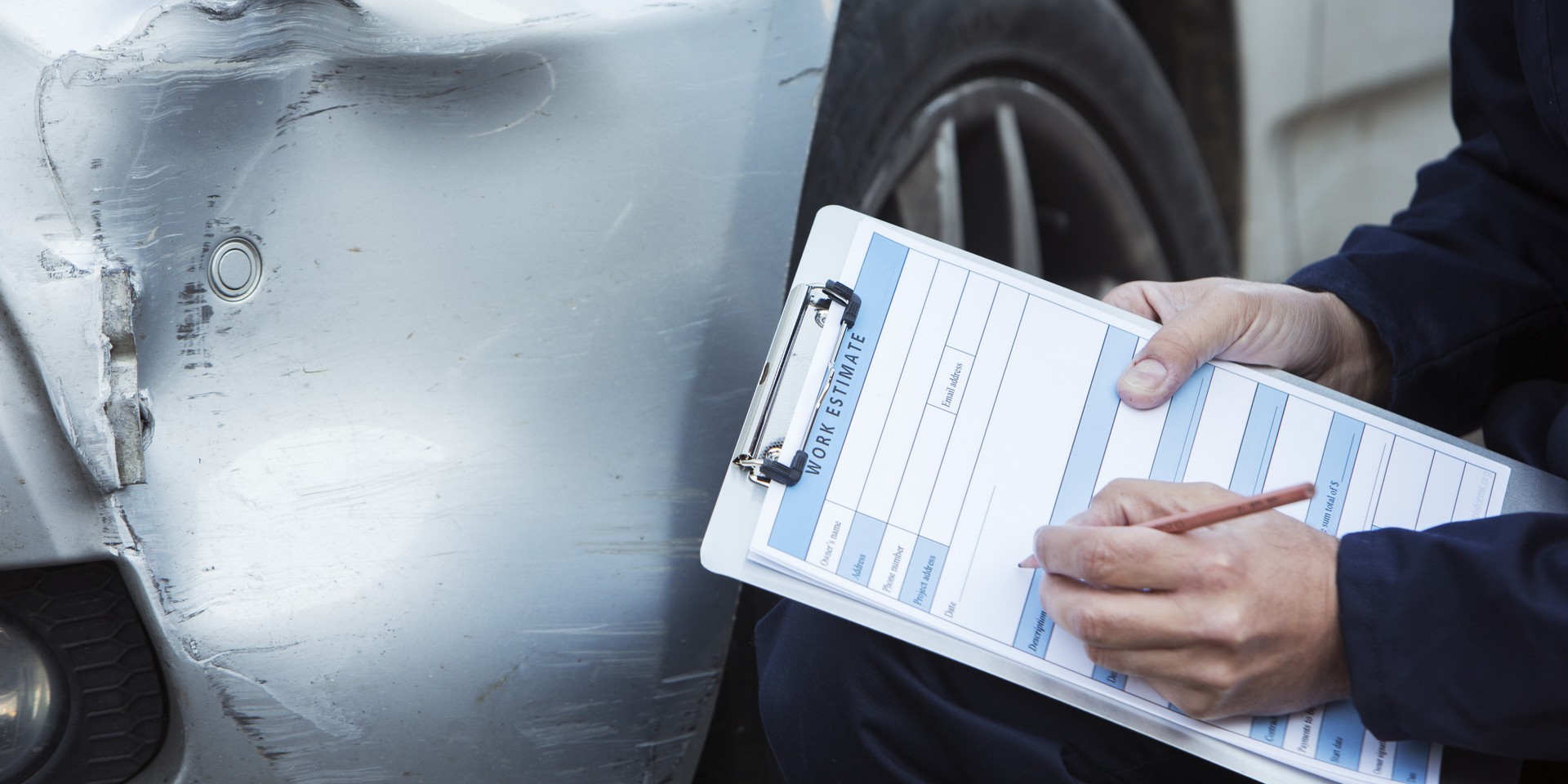 Auto Workshop Mechanic Inspecting Damage To Car And Filling In R